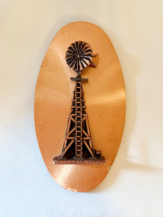 Decorative wall art with a windmill design on a copper-colored oval background