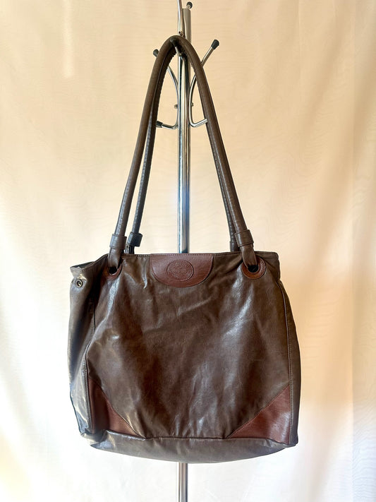 Brown leather handbag hanging on a coat rack against a beige background